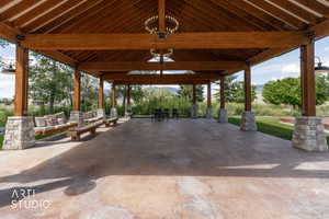 Expansive covered patio featuring a wood-beam ceiling, stone-wrapped columns, concrete flooring, and built-in swing seating