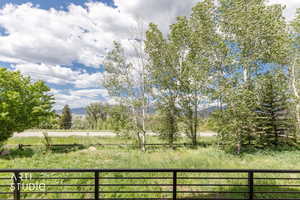 Expansive outdoor scenery featuring mature trees, a grassy field, and distant mountains under a blue sky with white clouds