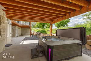 Covered patio area featuring a built-in spa with steps, exposed wood beam ceiling, stone accent wall, and concrete flooring