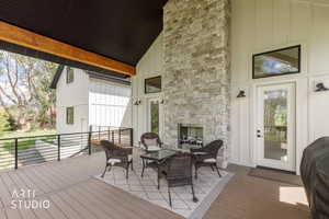 Covered outdoor living area featuring a stone fireplace, durable composite decking, board and batten siding, substantial exposed wood beam, and black metal railings