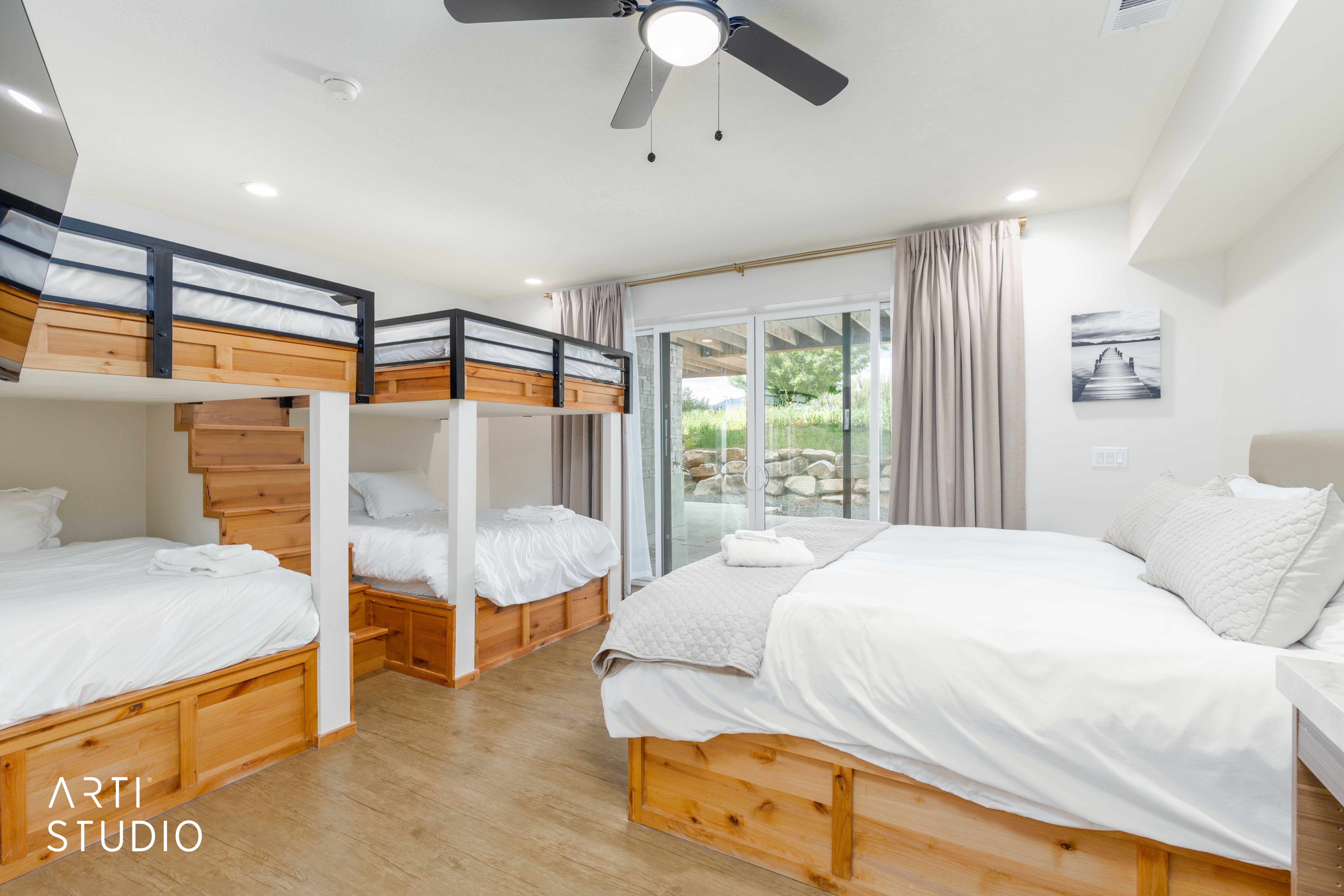 Spacious room featuring multiple built-in bunk beds with integrated storage, a large bed with under-bed storage, wood-finish flooring, a ceiling fan, and recessed lighting