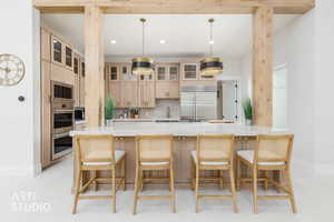 Spacious kitchen featuring a large central island with seating, natural wood cabinetry, integrated stainless steel appliances, marble countertops, and decorative pendant lighting