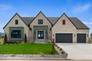 Stone facade residence featuring a prominent entryway with double glass-paneled doors, two attached garages with dark paneled doors, a large bay window with dark trim, and a manicured lawn with landscape rock accents