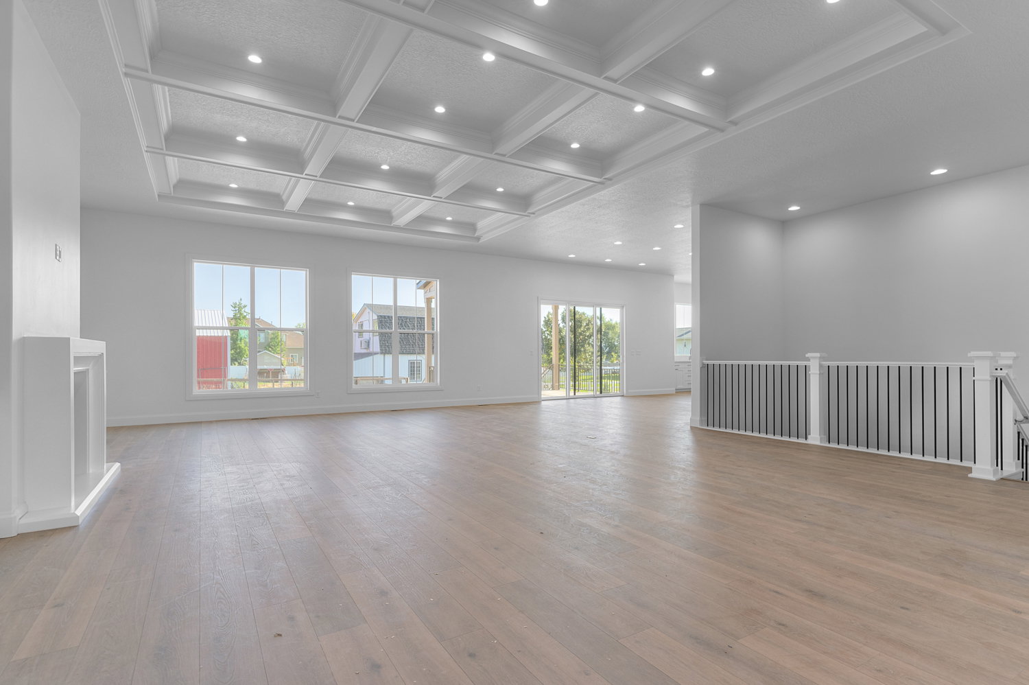 Spacious interior featuring coffered ceilings with recessed lighting, light wood-finish flooring, multiple windows, a built-in fireplace mantle, and a staircase with a railing