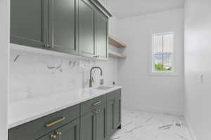 Laundry room with dark green cabinetry, white countertop, marble-look tile backsplash, and a window providing natural light