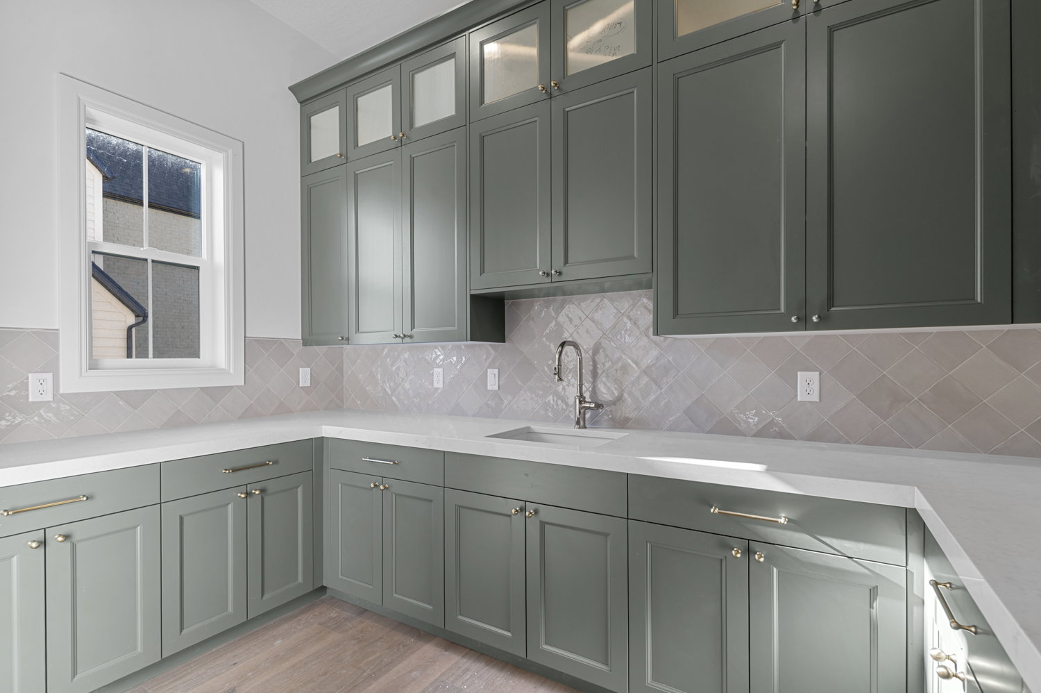 Kitchenette featuring sage green cabinetry, white countertops, square grid window, light-toned backsplash, and wood-finish flooring