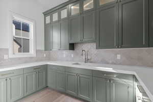 Kitchenette featuring sage green cabinetry, white countertops, square grid window, light-toned backsplash, and wood-finish flooring