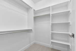 Walk-in closet featuring white built-in shelving, chrome hanging rods, matching baseboards, and neutral carpet flooring