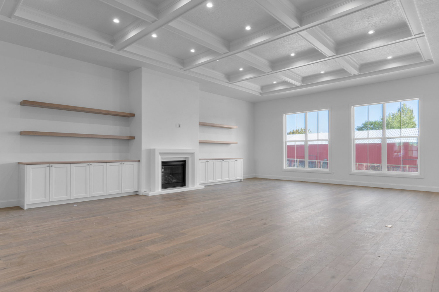 Spacious interior featuring a coffered ceiling with recessed lighting, light wood-finish flooring, and a fireplace with a white surround