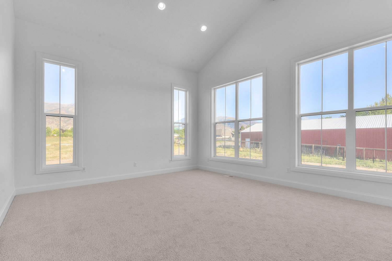 Vaulted ceiling room featuring recessed lighting, multiple large windows with white trim, light-colored carpeting, and white painted walls