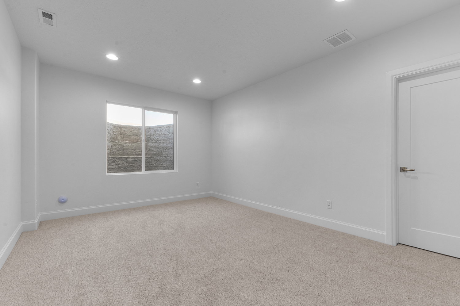 Bright room featuring soft carpet flooring, recessed ceiling lighting, a white painted door with contemporary hardware, and a window with a stone-textured exterior wall