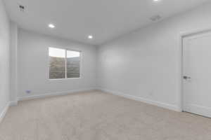 Bright room featuring soft carpet flooring, recessed ceiling lighting, a white painted door with contemporary hardware, and a window with a stone-textured exterior wall