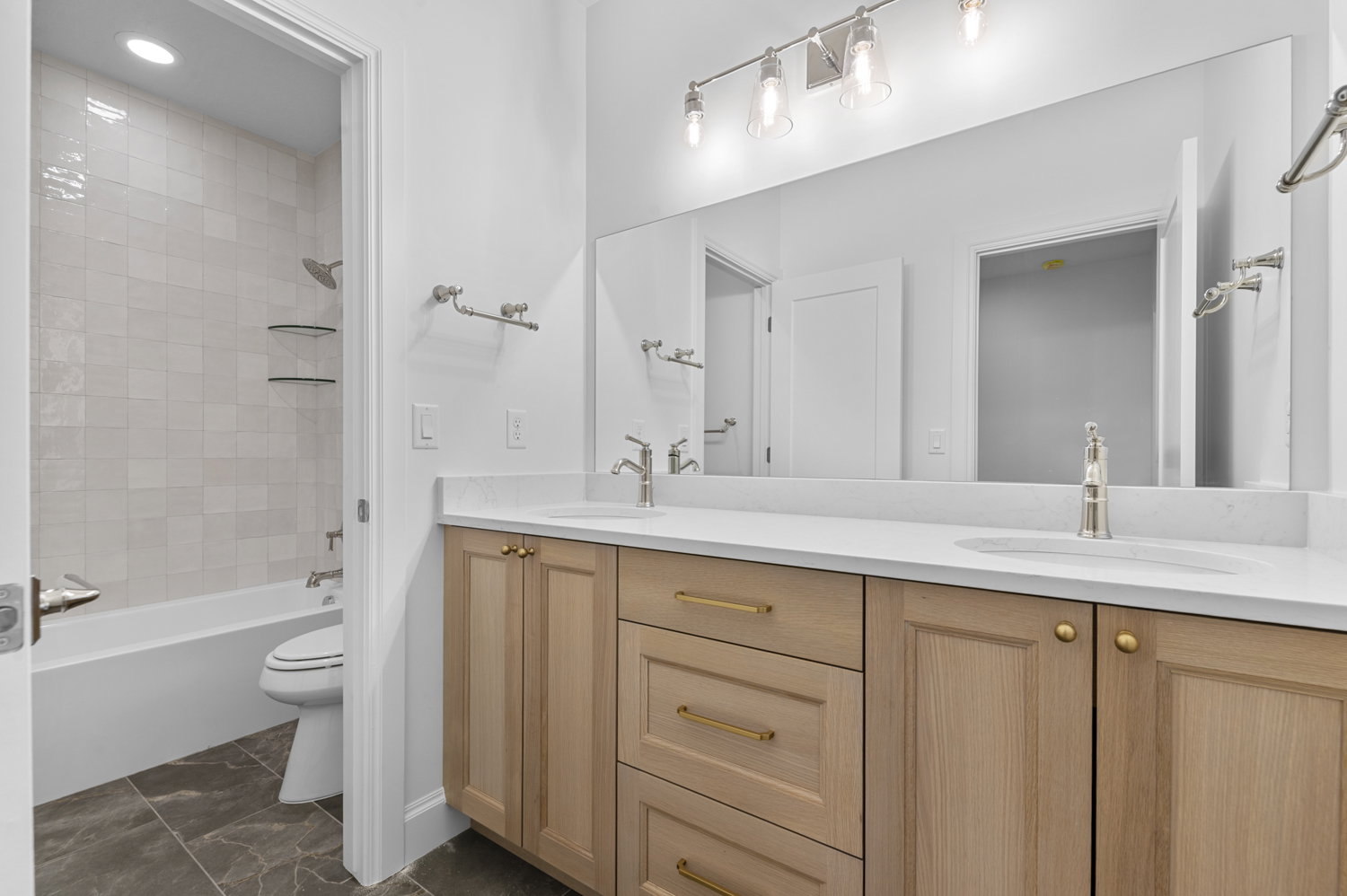 Contemporary bathroom featuring a double vanity with light wood cabinetry, white countertops, and dual undermount sinks