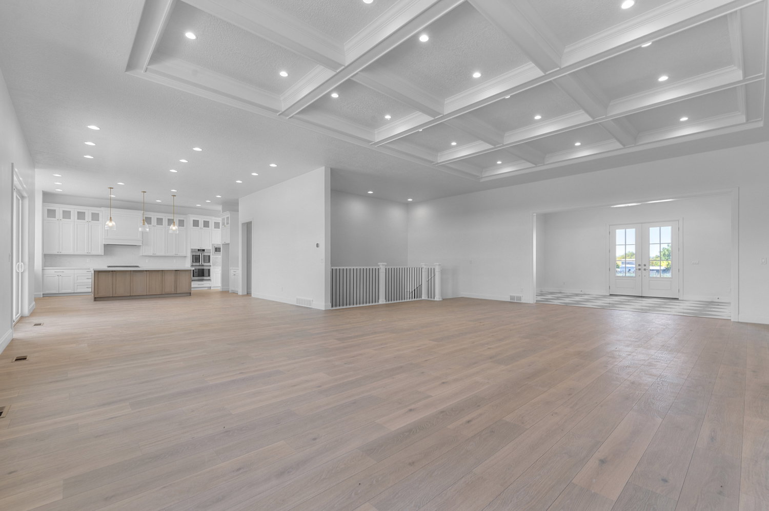 Expansive open-concept living space featuring light wood-finish flooring, a coffered ceiling with recessed lighting, and a modern kitchen