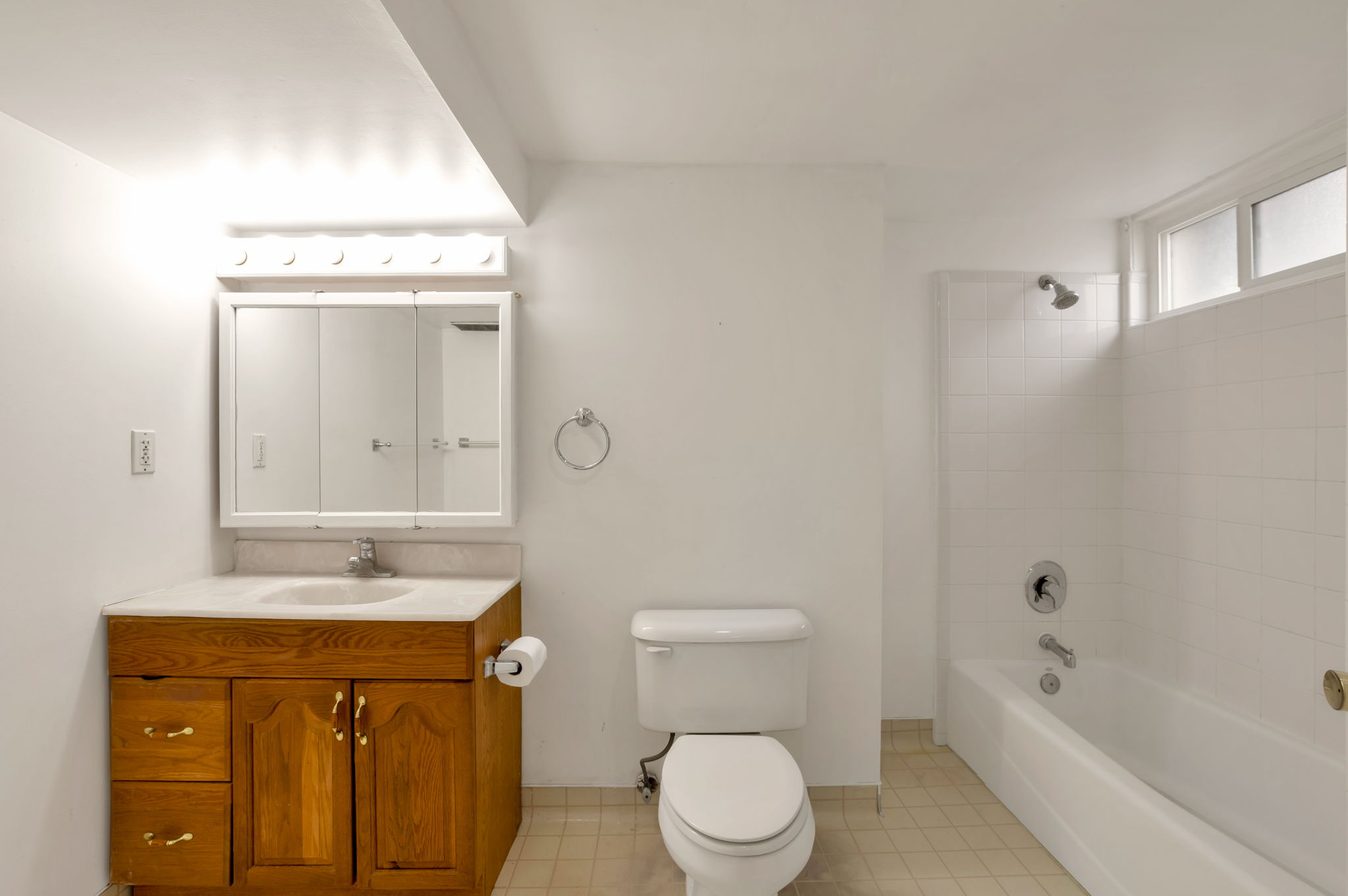 Bathroom featuring a wood-finish vanity with a built-in sink, a wall-mounted medicine cabinet with integrated mirror, and a full bathtub with a tiled shower surround