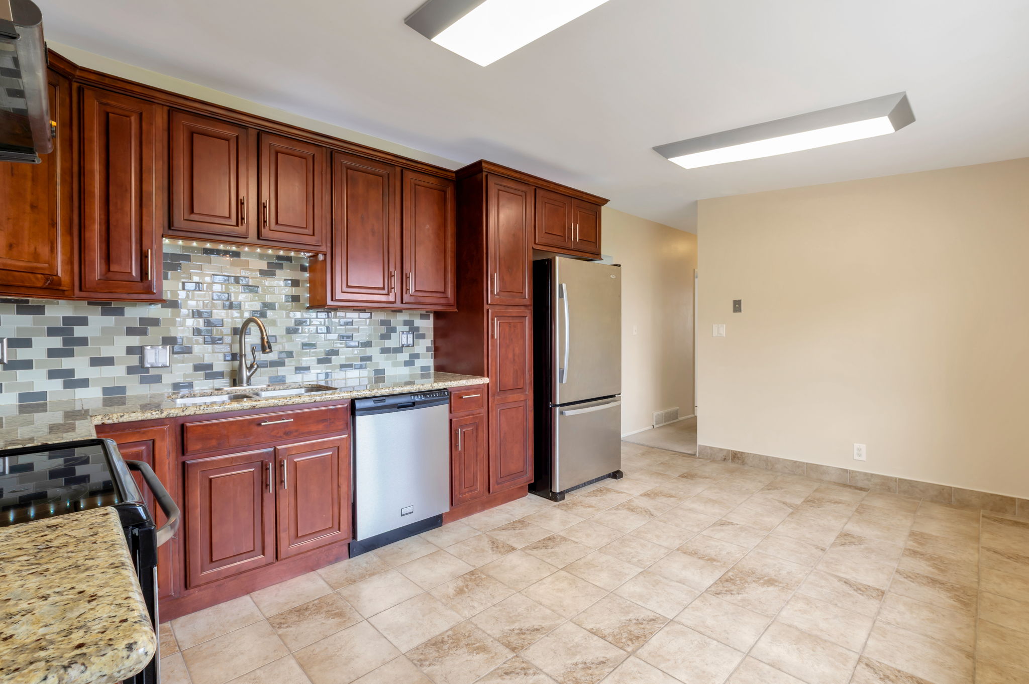 Kitchen featuring dark wood cabinetry, stainless steel appliances, granite countertops, and a mosaic tile backsplash