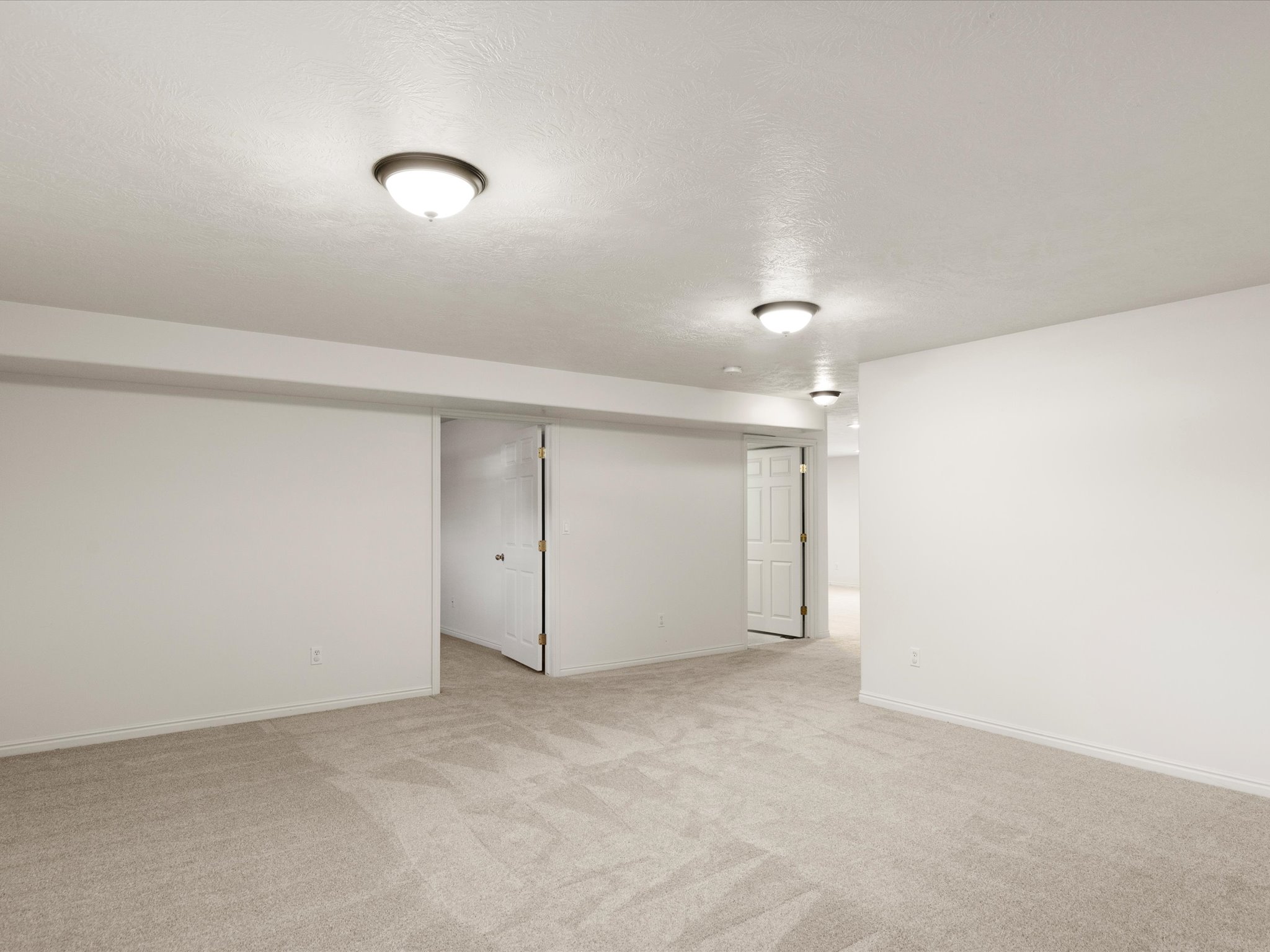 Spacious room featuring neutral carpeting, white walls, and bright overhead lighting