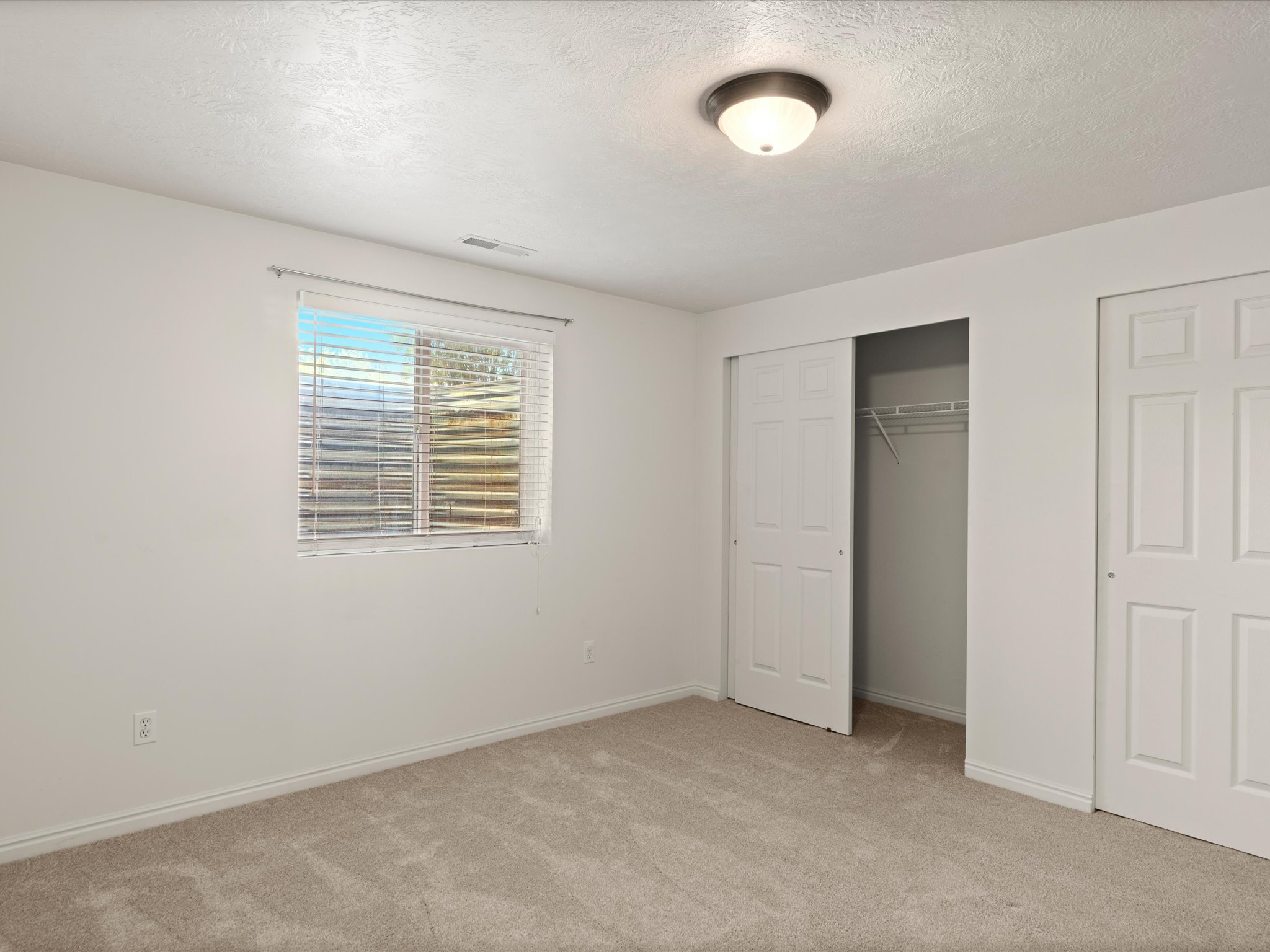 Carpeted room featuring a single window with blinds, white walls, and a ceiling-mounted light fixture