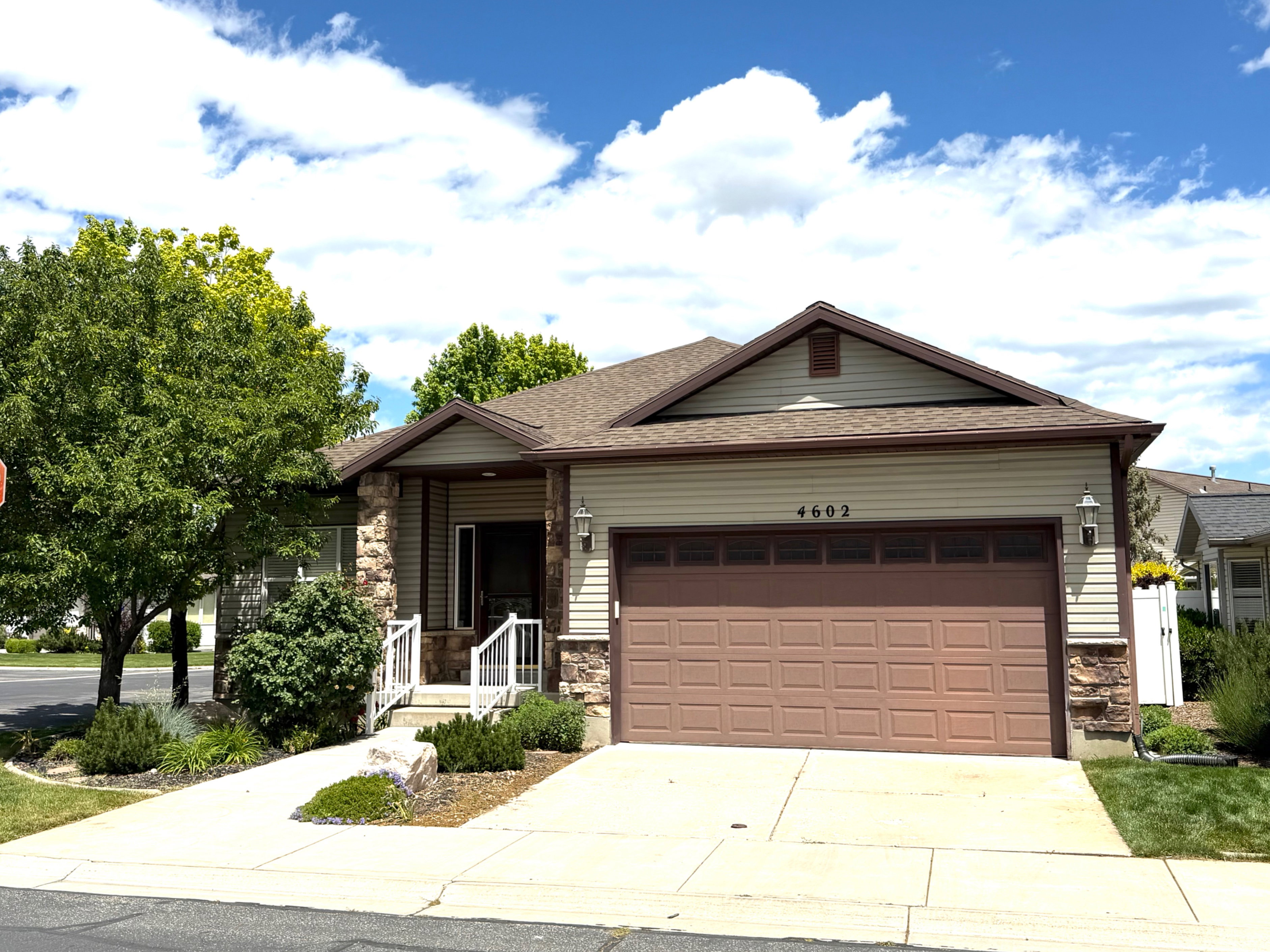 Single-story residence featuring a two-car garage with a brown panel door, light beige siding, and stone accents