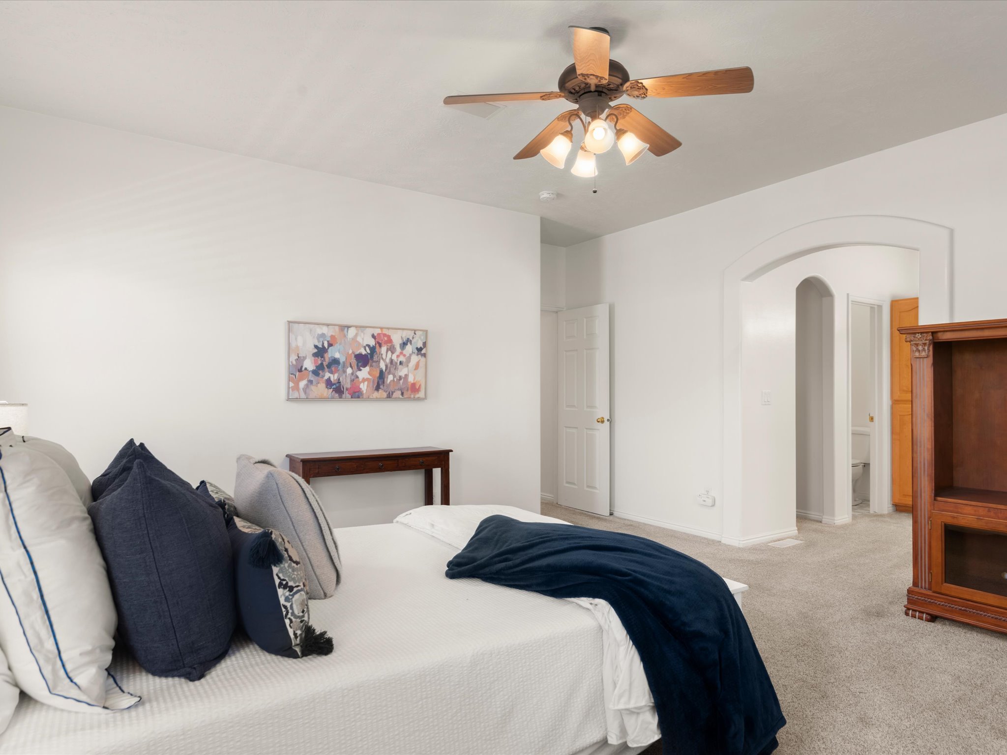 Spacious interior featuring a neutral color palette, ceiling fan with light fixture, carpet flooring, and an arched doorway leading to another room