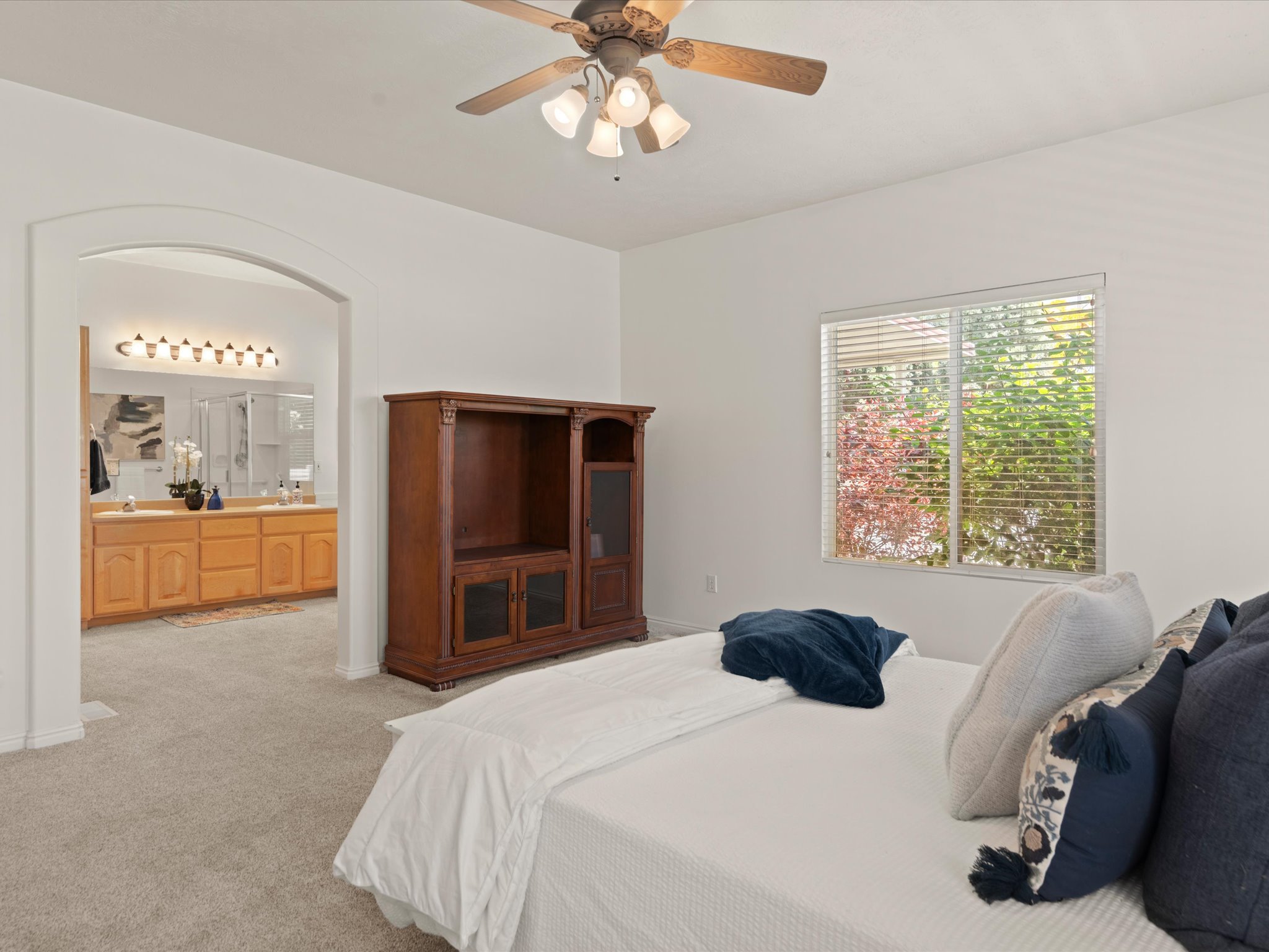 Carpeted bedroom featuring an arched doorway, ceiling fan with light kit, and a window with horizontal blinds