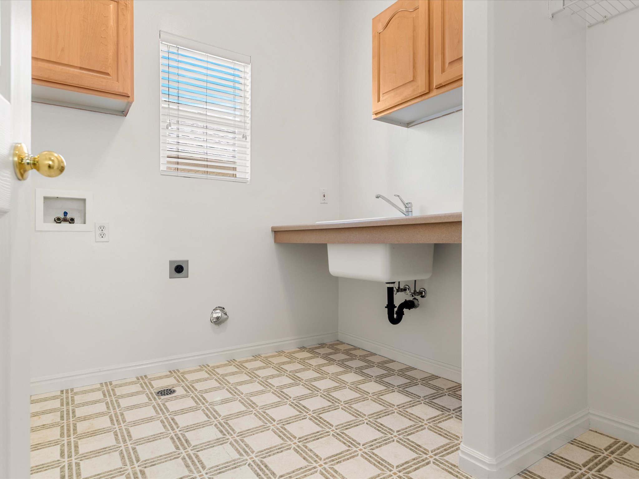 Utility room with patterned tile flooring, wood-finish cabinetry, and a built-in utility sink