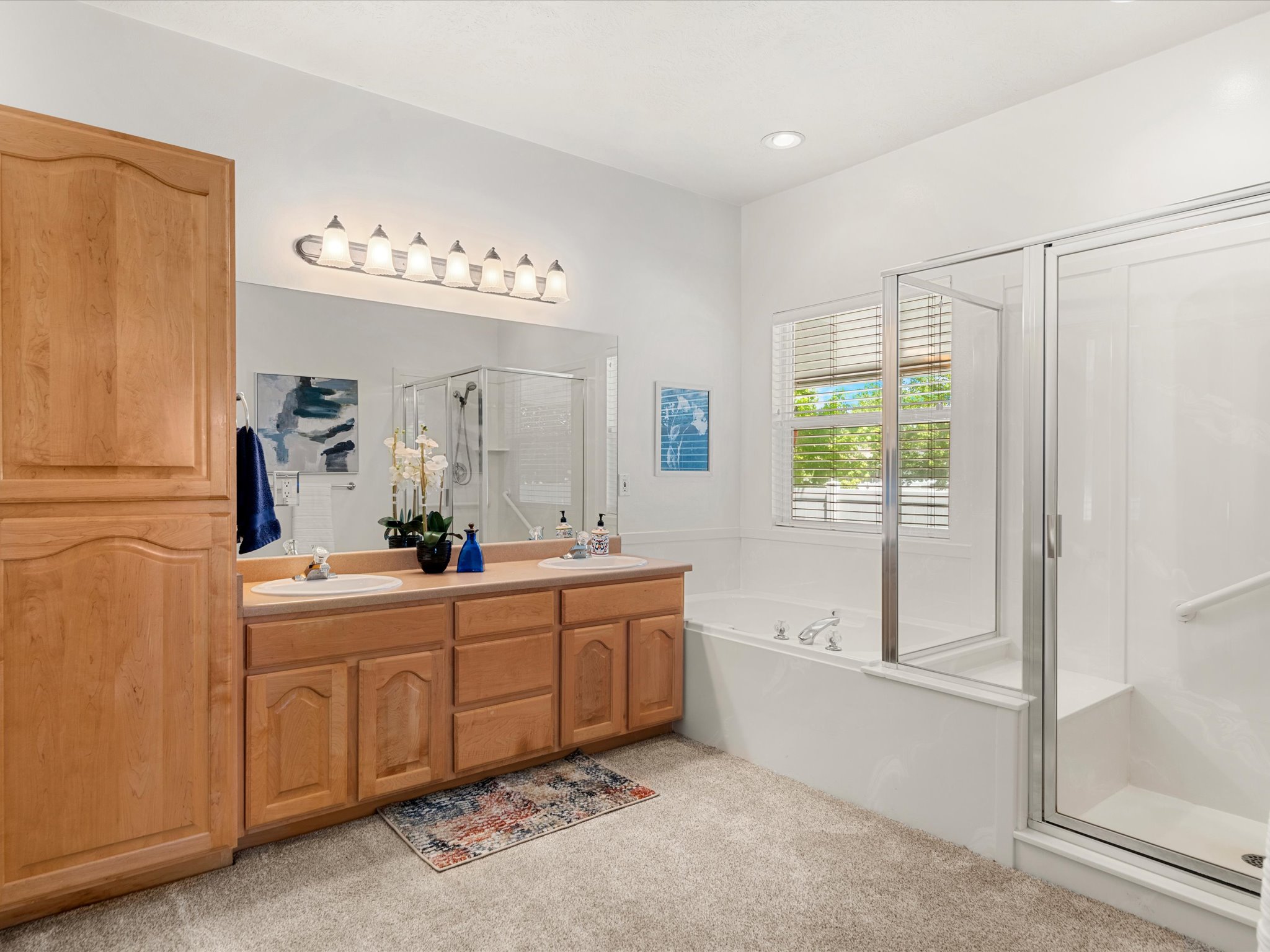 Bathroom featuring a double vanity with light wood cabinetry, a large mirror, and a seven-light fixture