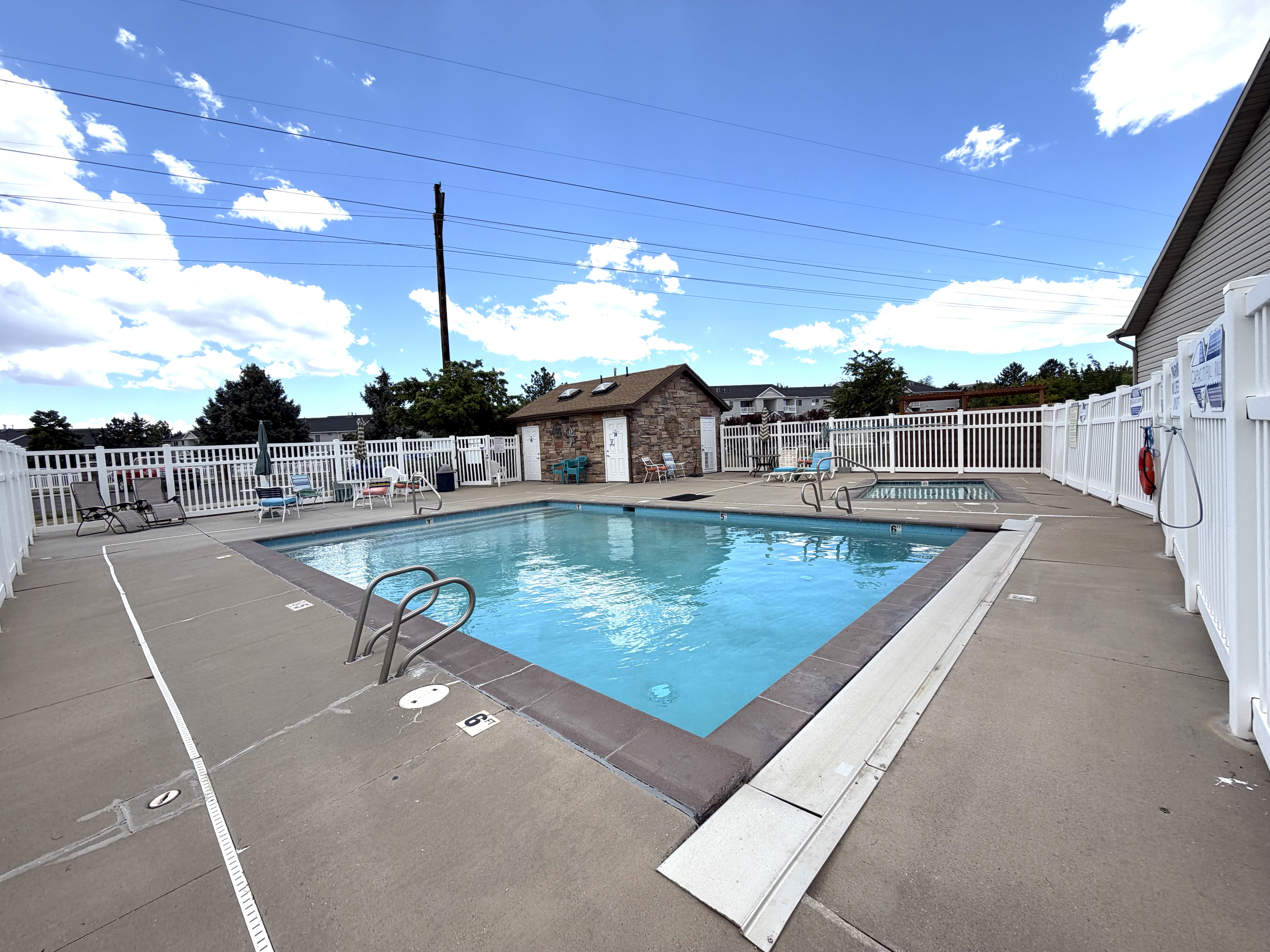 Community swimming pool featuring a concrete deck and white privacy fencing