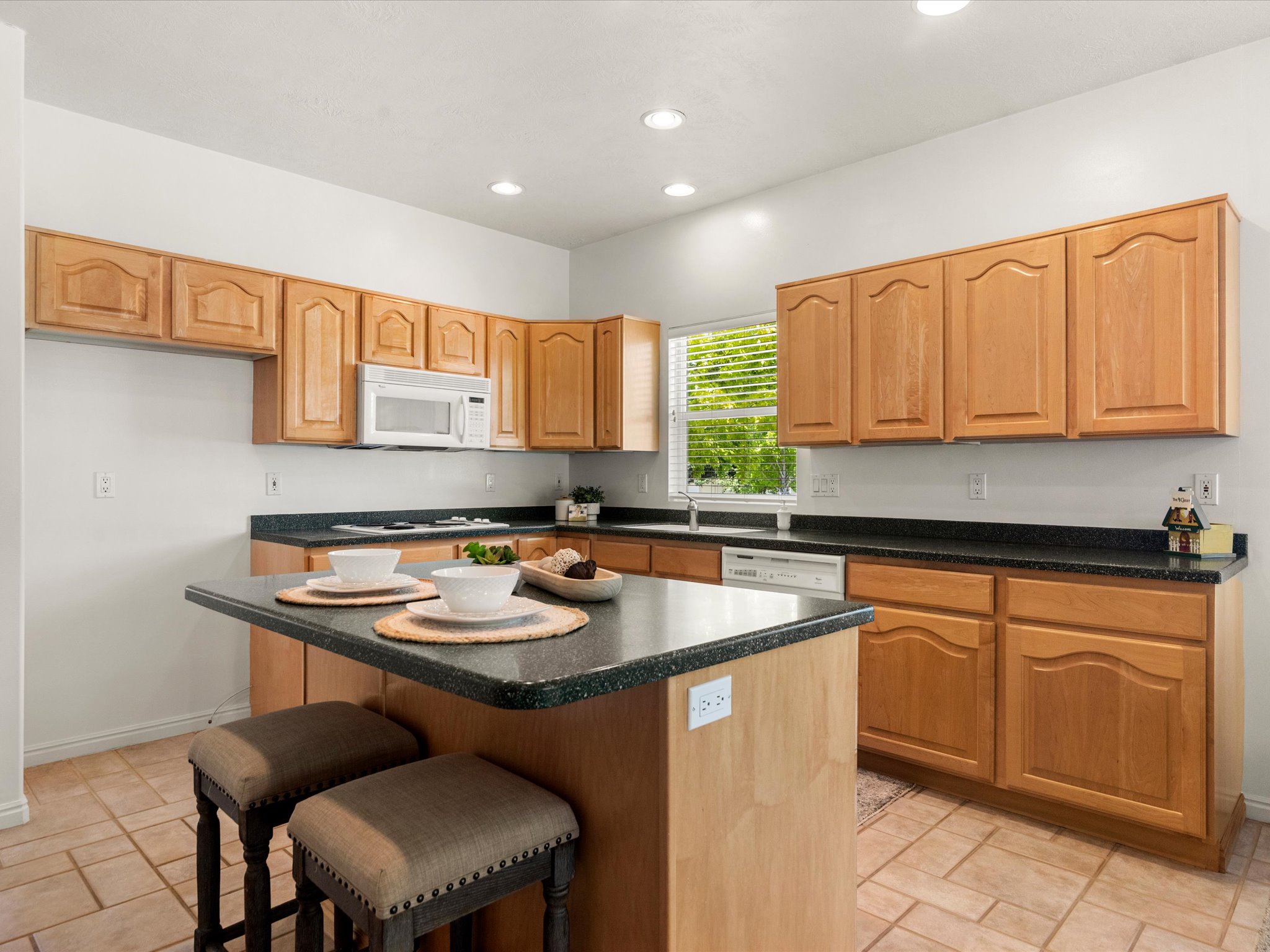 Kitchen featuring light wood cabinetry with arched panel doors, dark speckled countertops, a center island with bar seating, a built-in microwave, and tile flooring