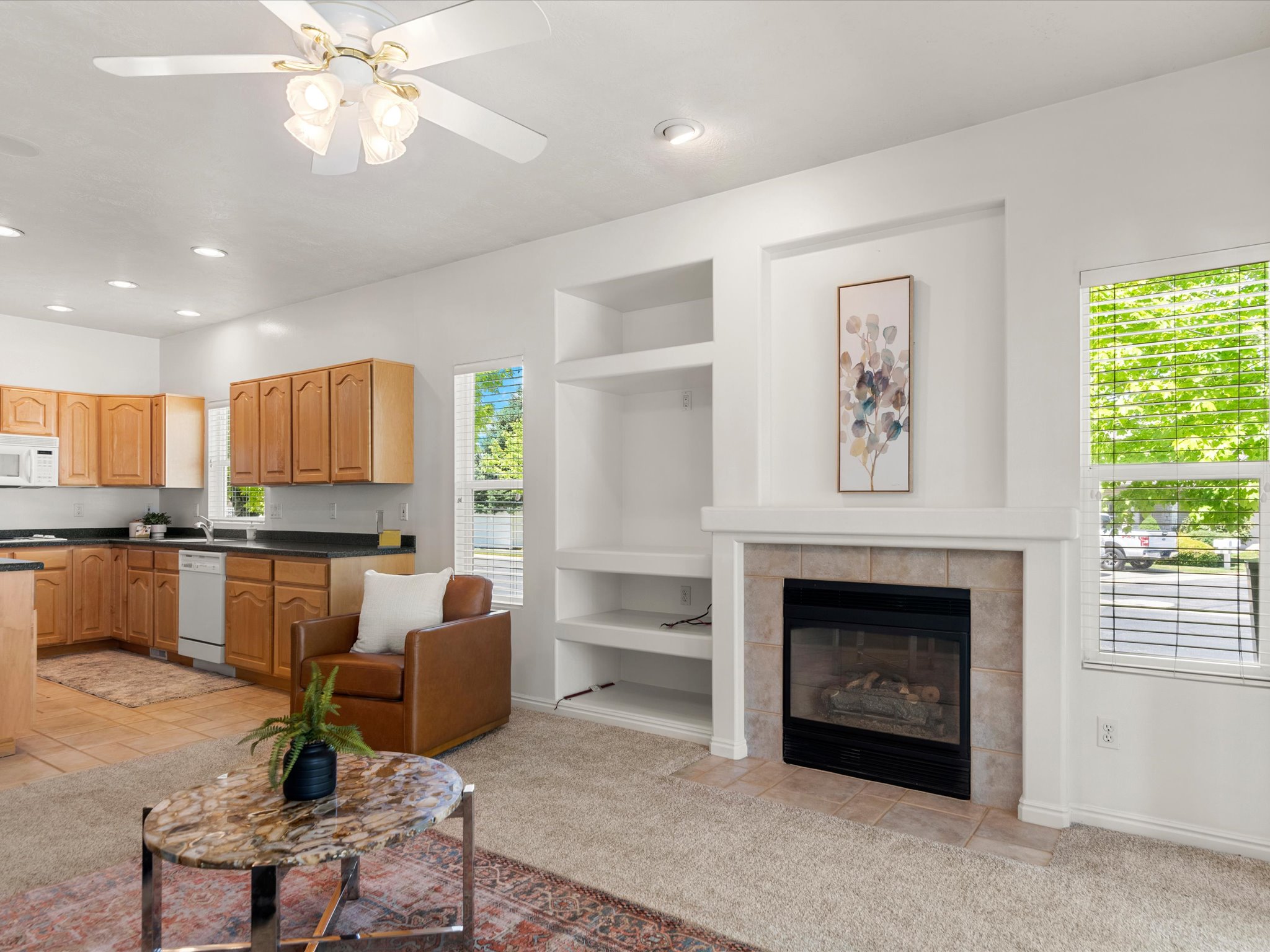 Living area featuring a tiled fireplace with mantel, built-in shelving, and a ceiling fan with integrated lighting