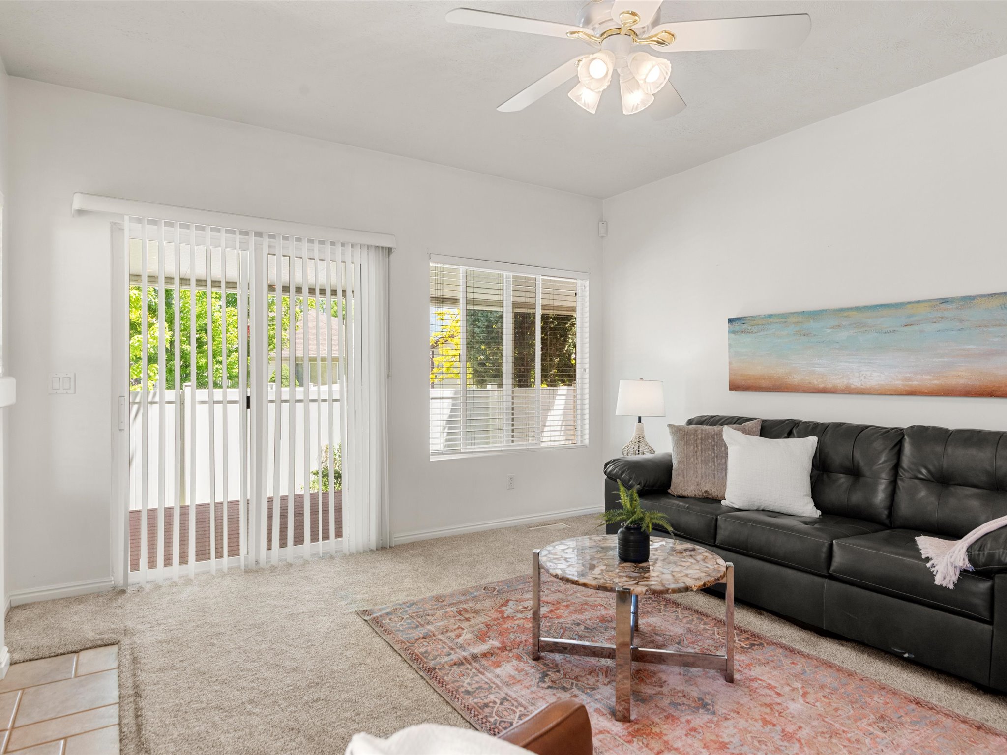 Carpeted living area featuring a sliding glass door, a window with blinds, and a ceiling fan with light fixture