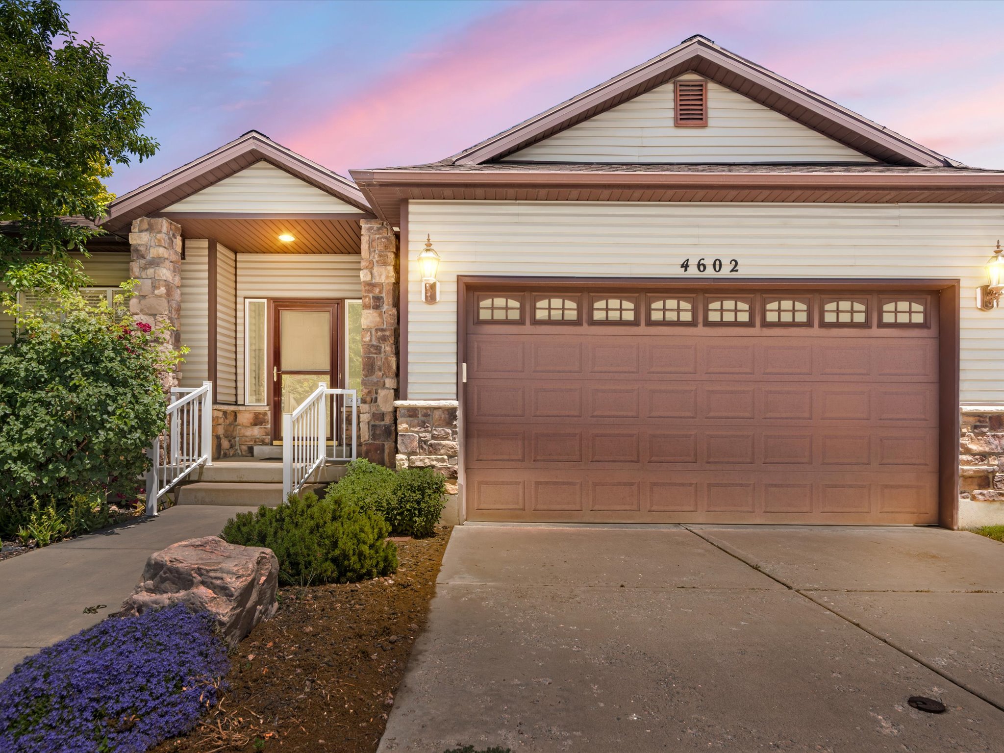 Exterior featuring a two-car garage with arched window inserts, stone accents, and light-colored siding