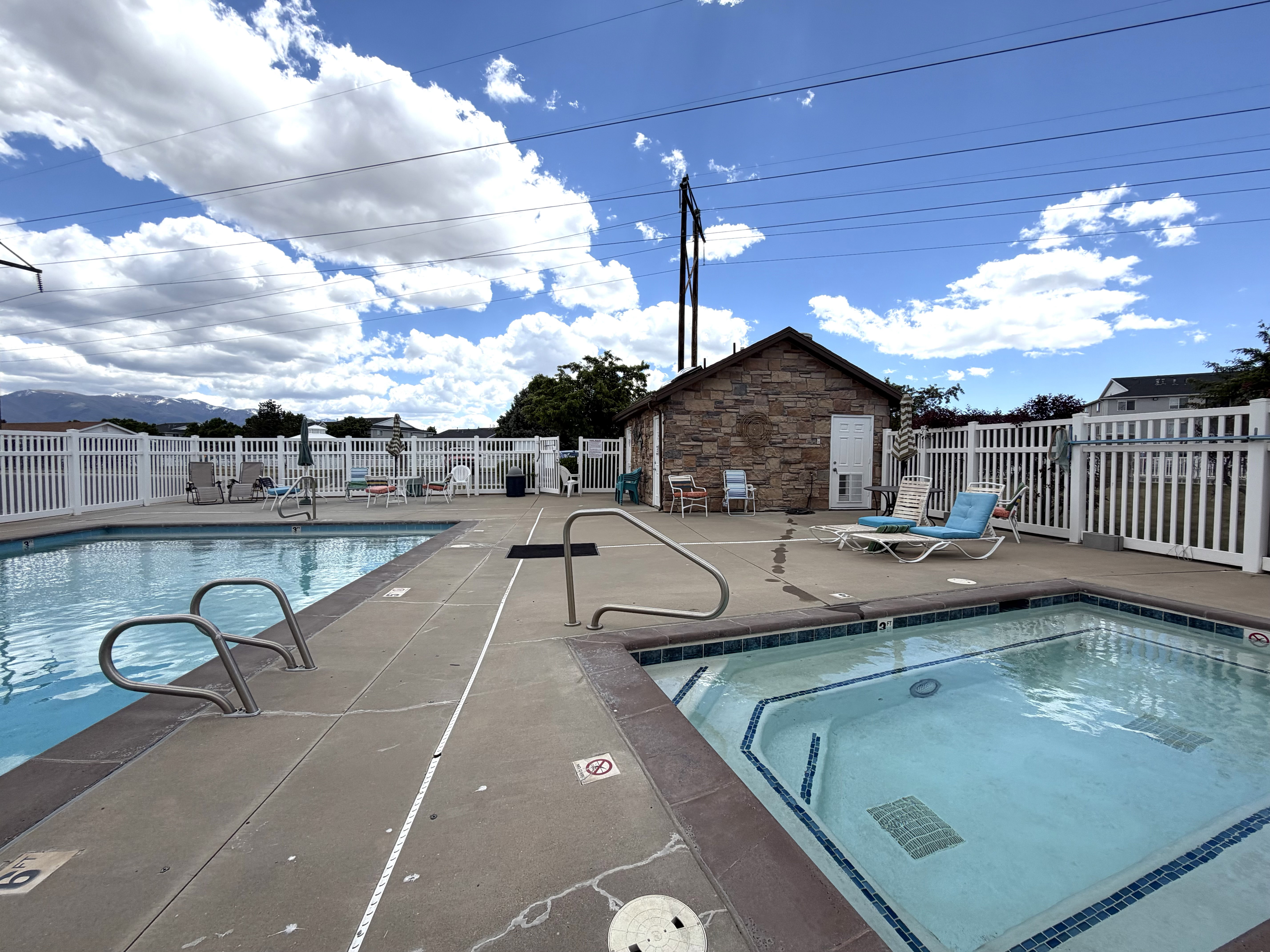 Outdoor swimming pool and spa area featuring a stone-clad building, white picket fencing, and concrete decking