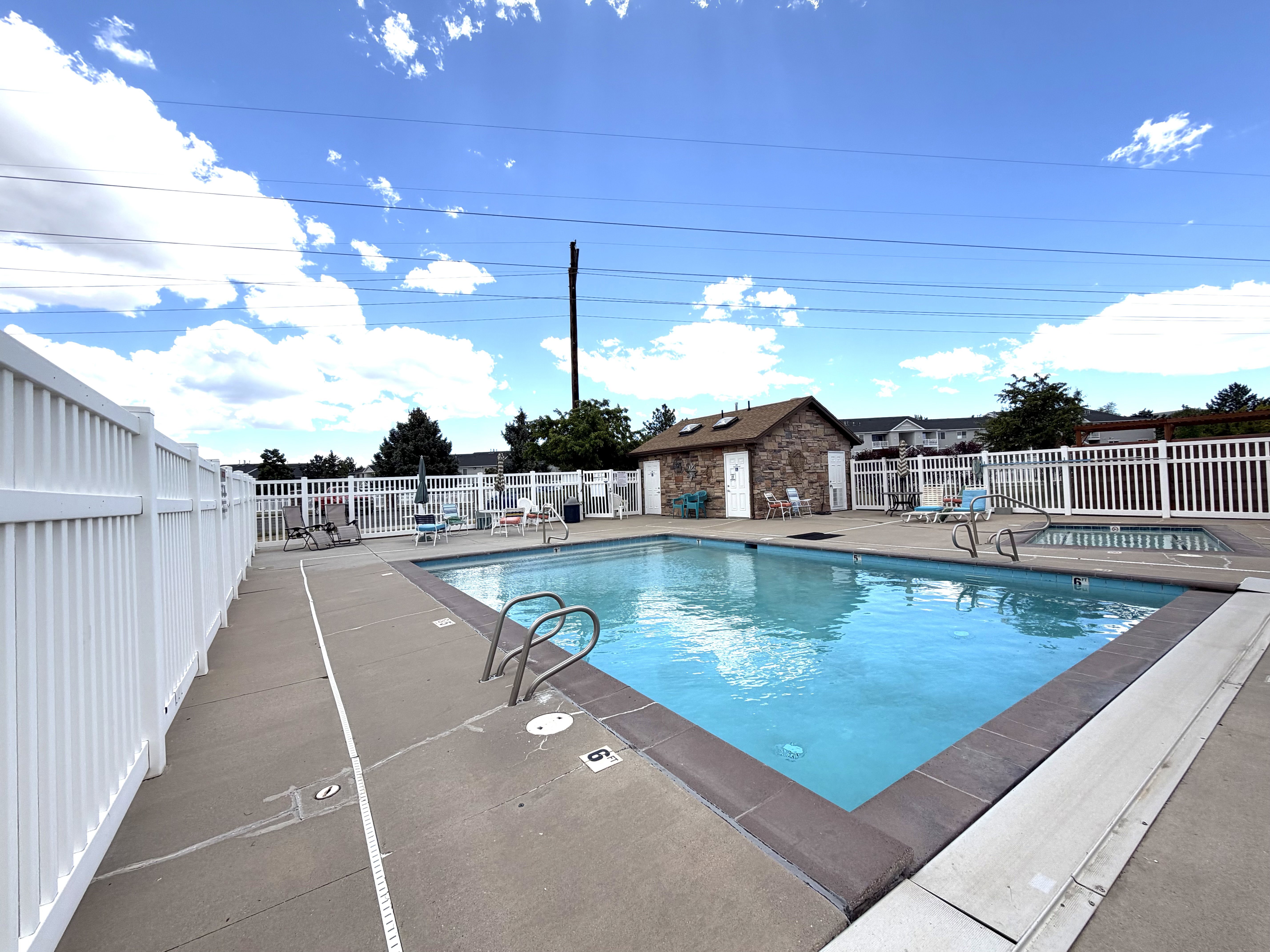 Community swimming pool featuring a concrete deck and white privacy fencing