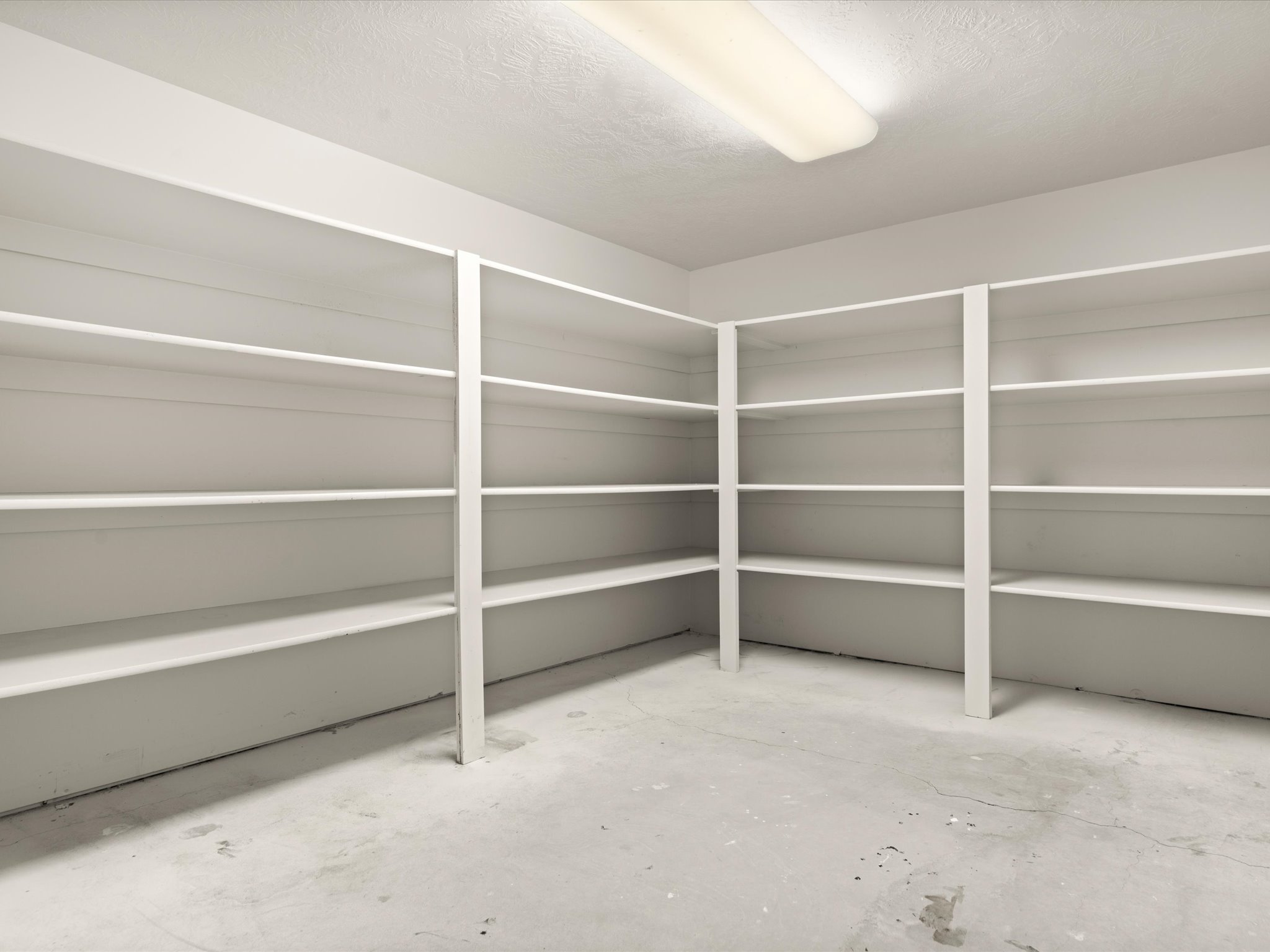 Spacious utility room featuring extensive built-in white shelving, a neutral concrete floor, and overhead fluorescent lighting