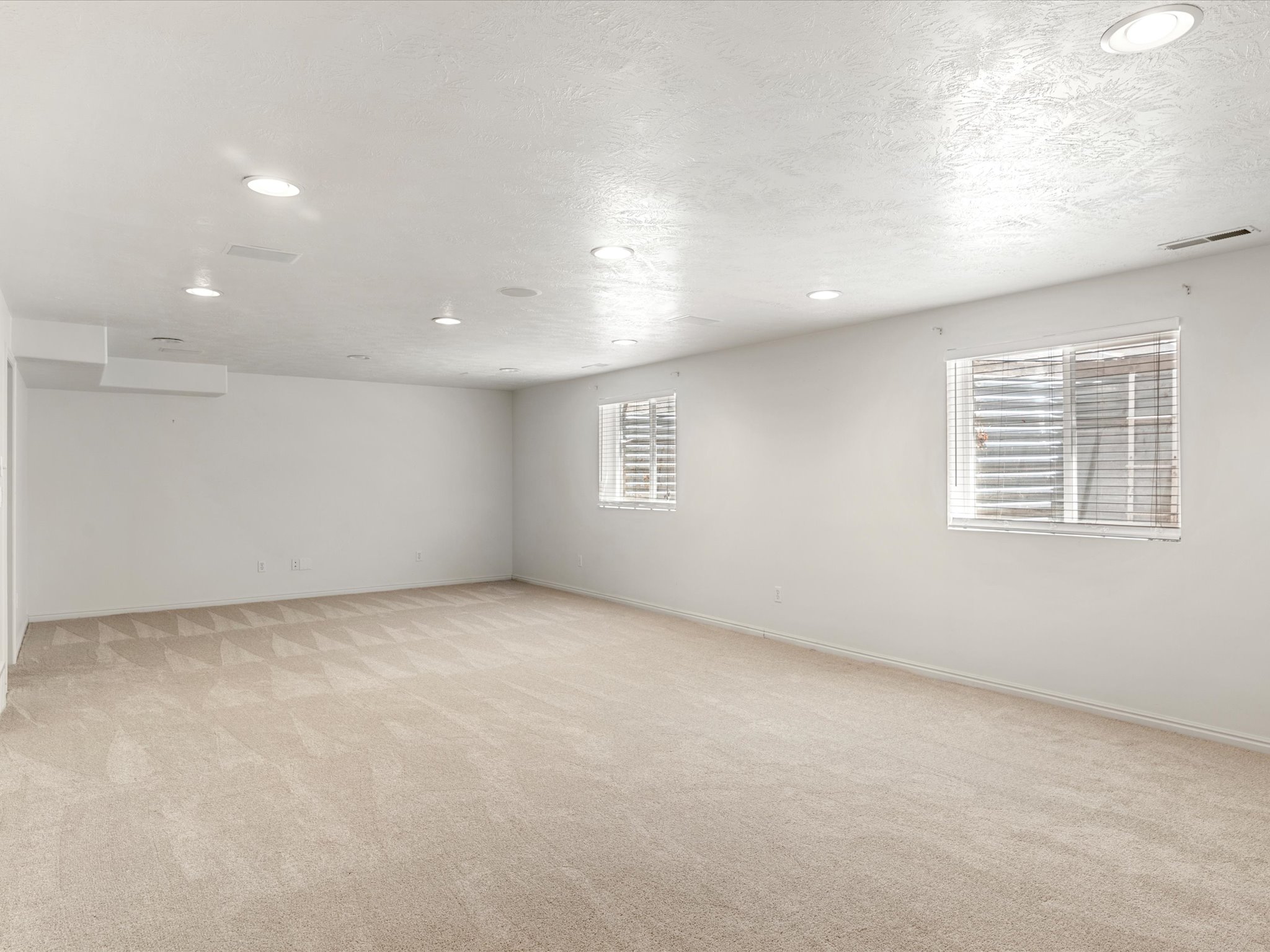 Spacious interior room featuring light-toned carpeting, white walls, and recessed lighting