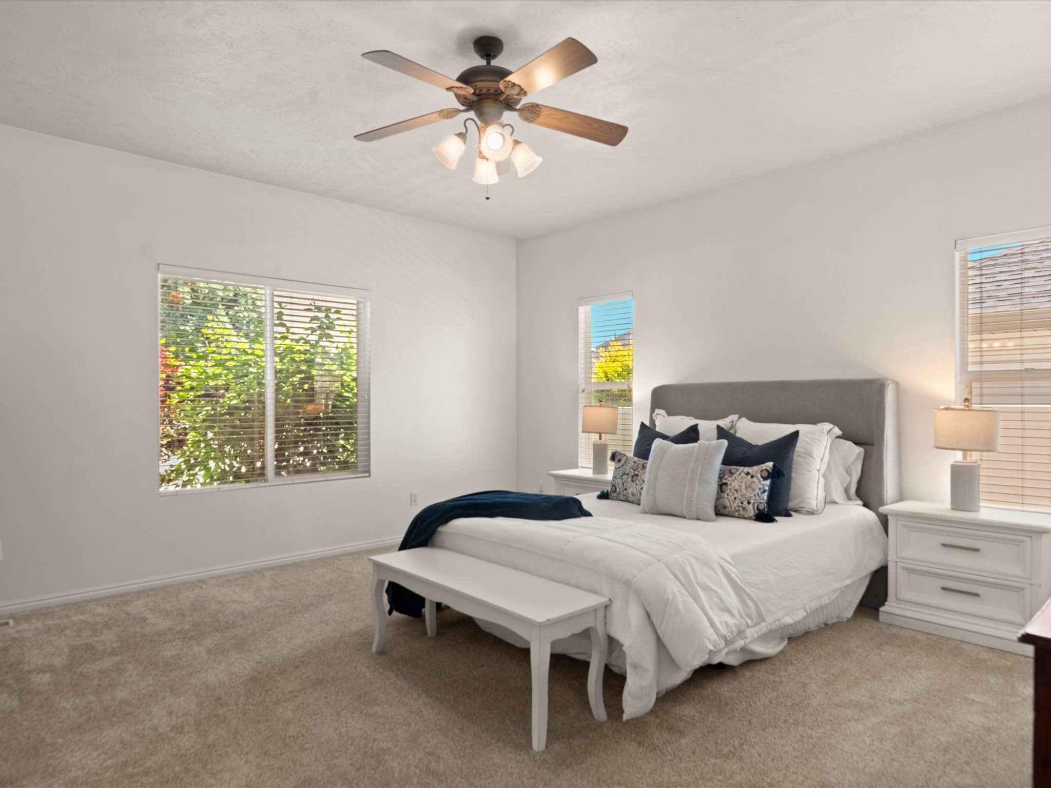 Carpeted bedroom featuring multiple windows, a ceiling fan with integrated lighting, and neutral wall tones