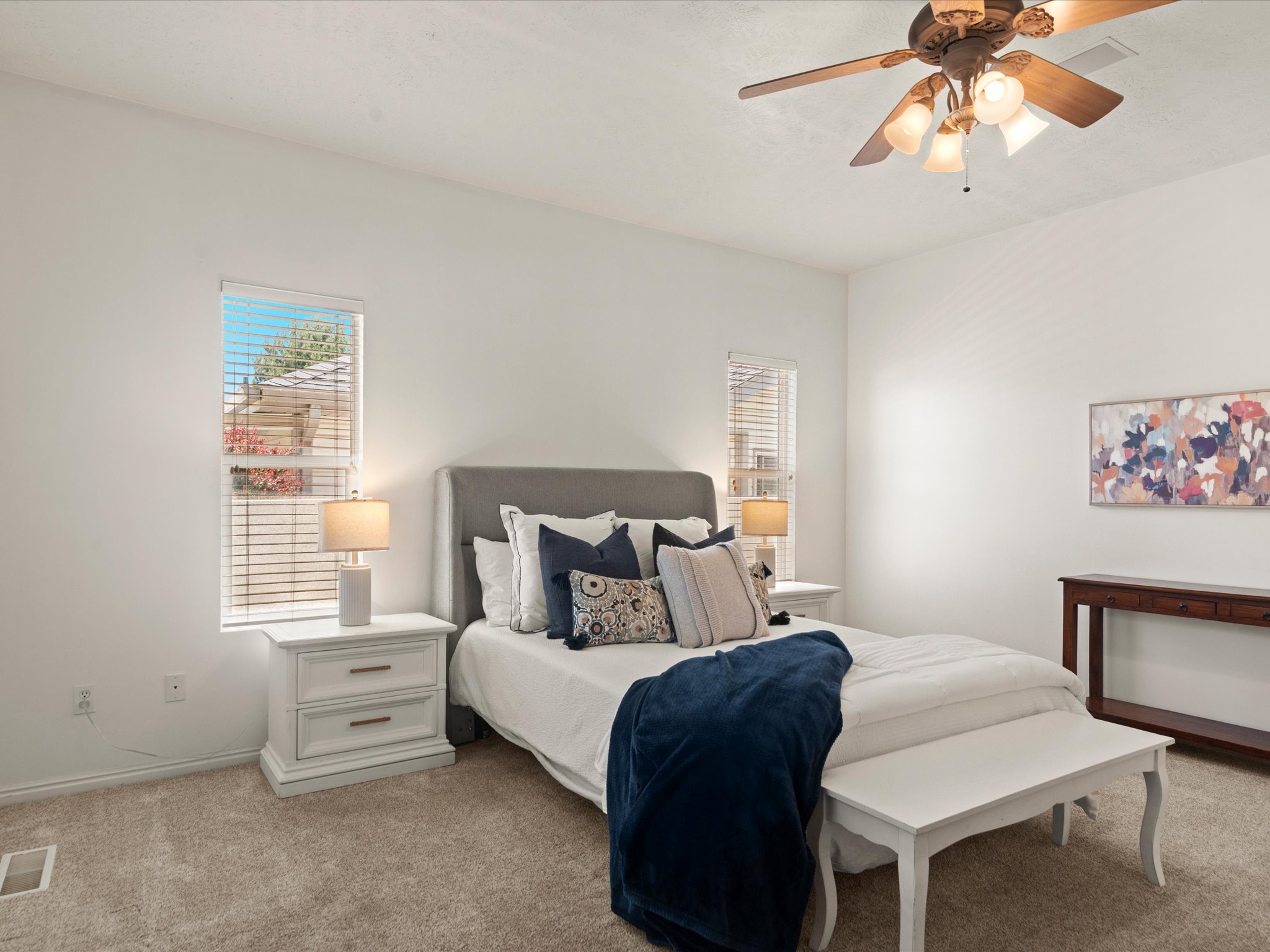 Carpeted room featuring two windows with blinds, a ceiling fan with integrated lighting, and white walls