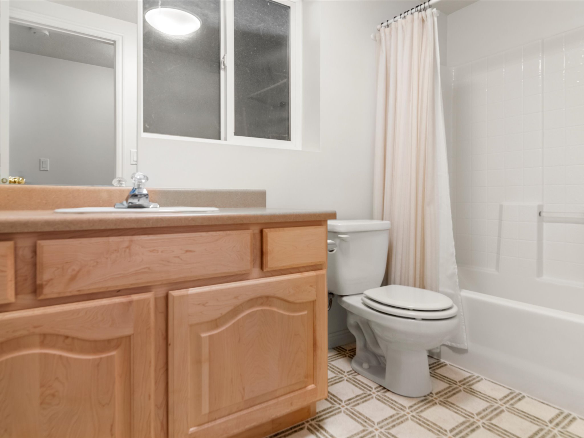Bathroom featuring a light wood-finish vanity with an integrated sink, patterned floor tiling, and a white bathtub with tile surround