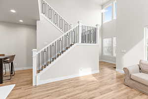 Two-story entry featuring light wood-finish flooring, a contemporary staircase with white balusters and black metal spindles, and high ceilings with upper windows