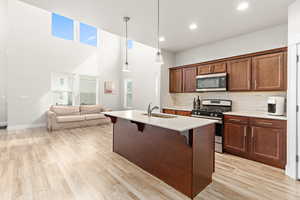 Open-concept living space with vaulted ceilings featuring high transom windows, wood-finish flooring, a kitchen island with sink, dark wood cabinetry, and a full suite of stainless steel appliances