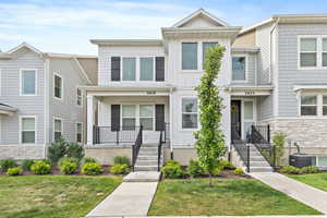 Modern townhome exterior featuring light-toned siding, dark shutters, and a covered porch