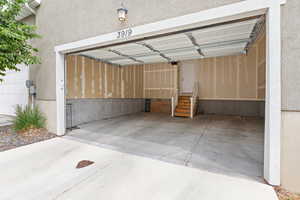 Two-car garage with concrete flooring, unfinished walls, and a separate entry door with wooden steps and a white handrail
