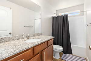 Bathroom featuring a single vanity with a granite-style countertop, an undermount sink, and wood-finish cabinetry