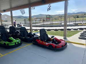 Covered outdoor staging area featuring multiple go-karts, a paved track bordered by tires, and distant mountainous terrain
