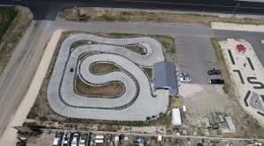 Aerial view showcasing a comprehensive entertainment property featuring a paved go-kart track with tire barriers, a building with a gray metal roof, a paved parking lot, and a distinct miniature golf course
