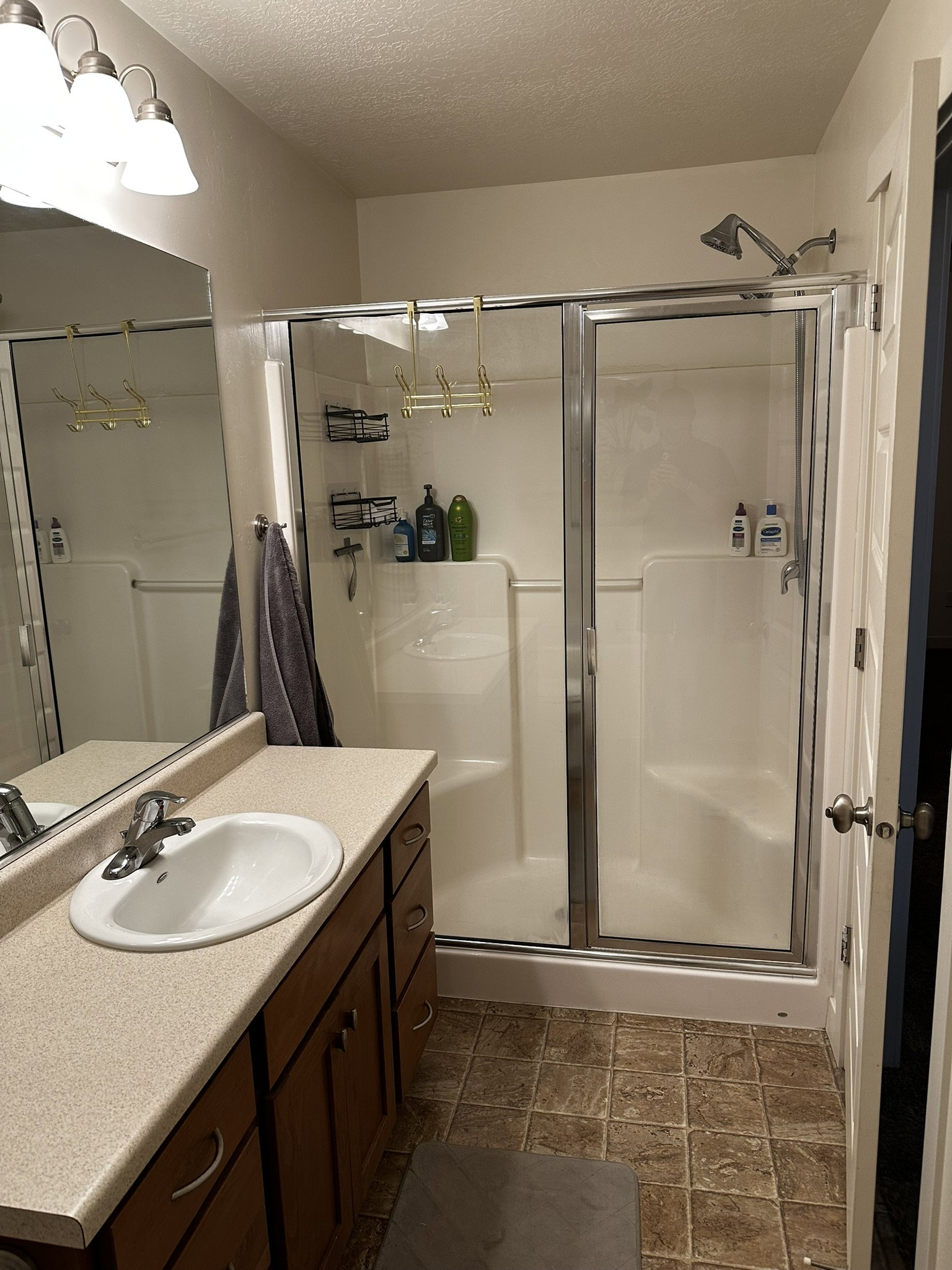Full bathroom featuring a shower with sliding glass doors, a vanity with a drop-in sink and a light-toned countertop, wood-finish cabinetry, and tiled flooring