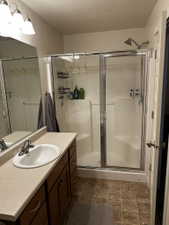 Full bathroom featuring a shower with sliding glass doors, a vanity with a drop-in sink and a light-toned countertop, wood-finish cabinetry, and tiled flooring