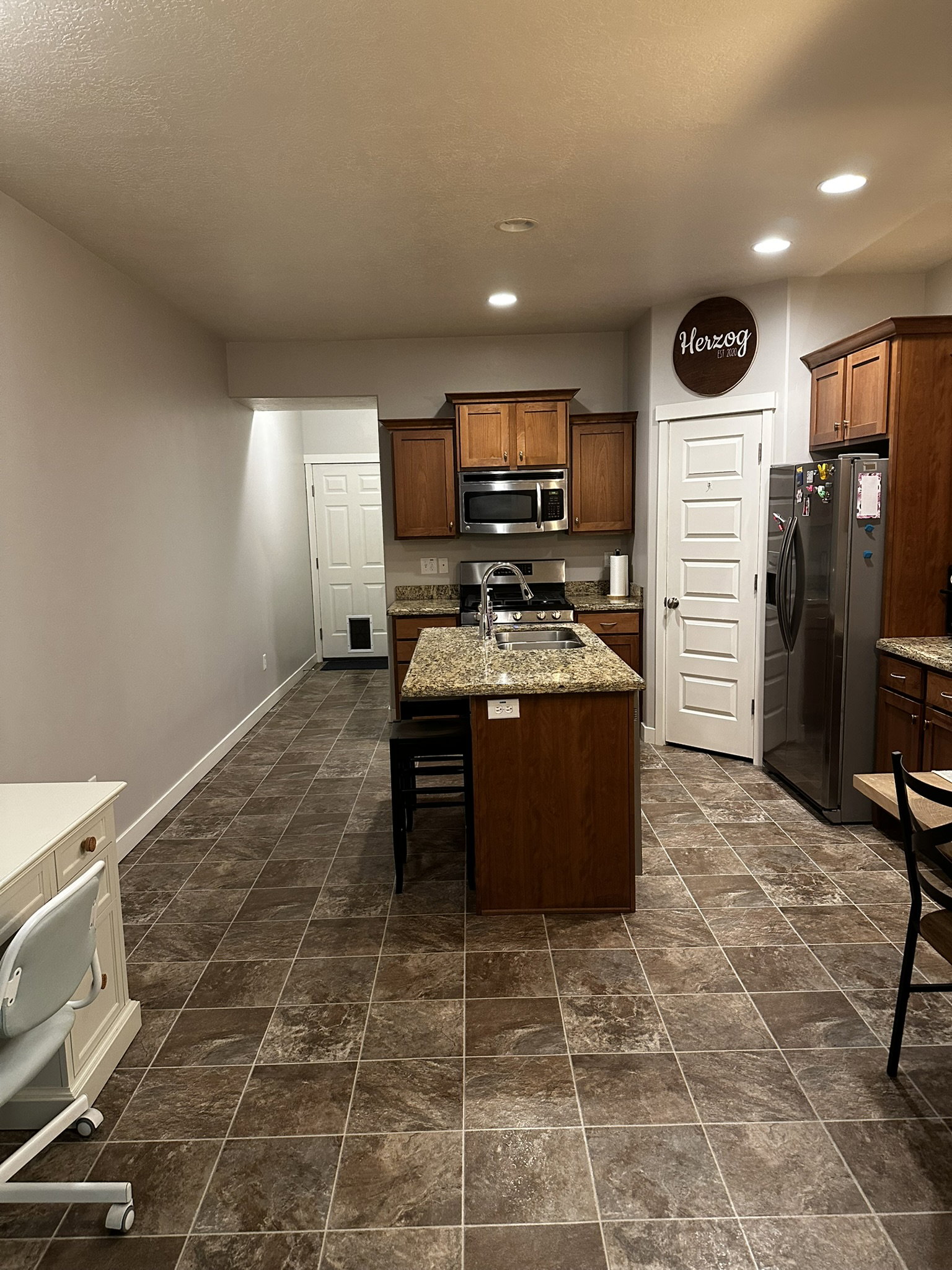 Kitchen featuring a central island with an undermount sink, stainless steel appliances, wood cabinetry, and a patterned tile floor