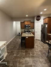 Kitchen featuring a central island with an undermount sink, stainless steel appliances, wood cabinetry, and a patterned tile floor